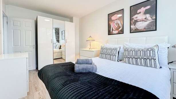 A modern bedroom with a large bed, a wardrobe, and a nightstand with a lamp.