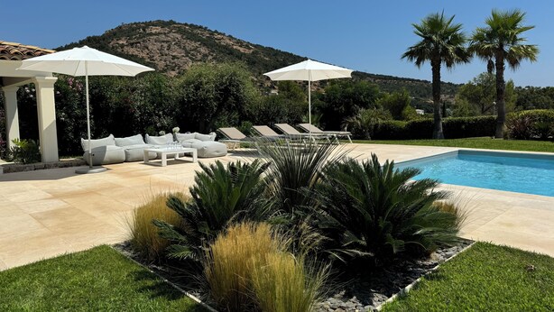 Zona de piscina con sillones de descanso, sombrillas y jardín ajardinado.