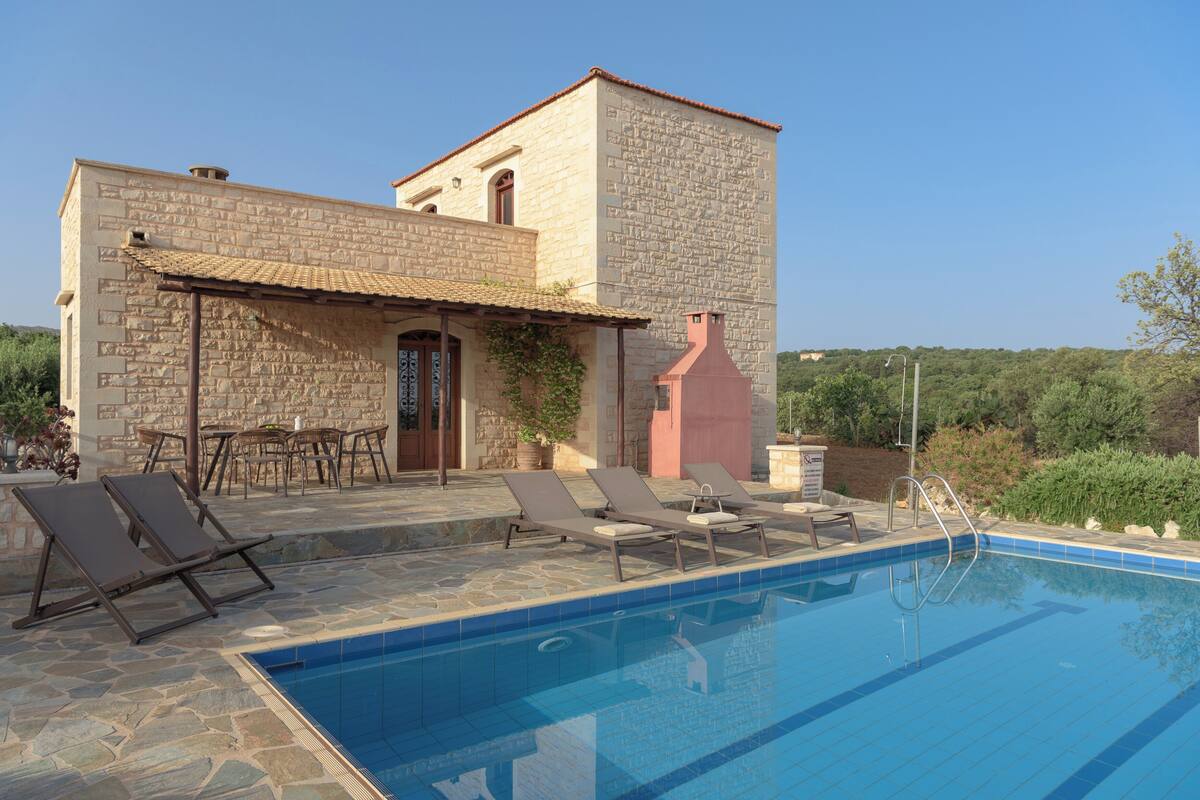 A stone building with a swimming pool, outdoor seating, and a clear view of the surrounding landscape.