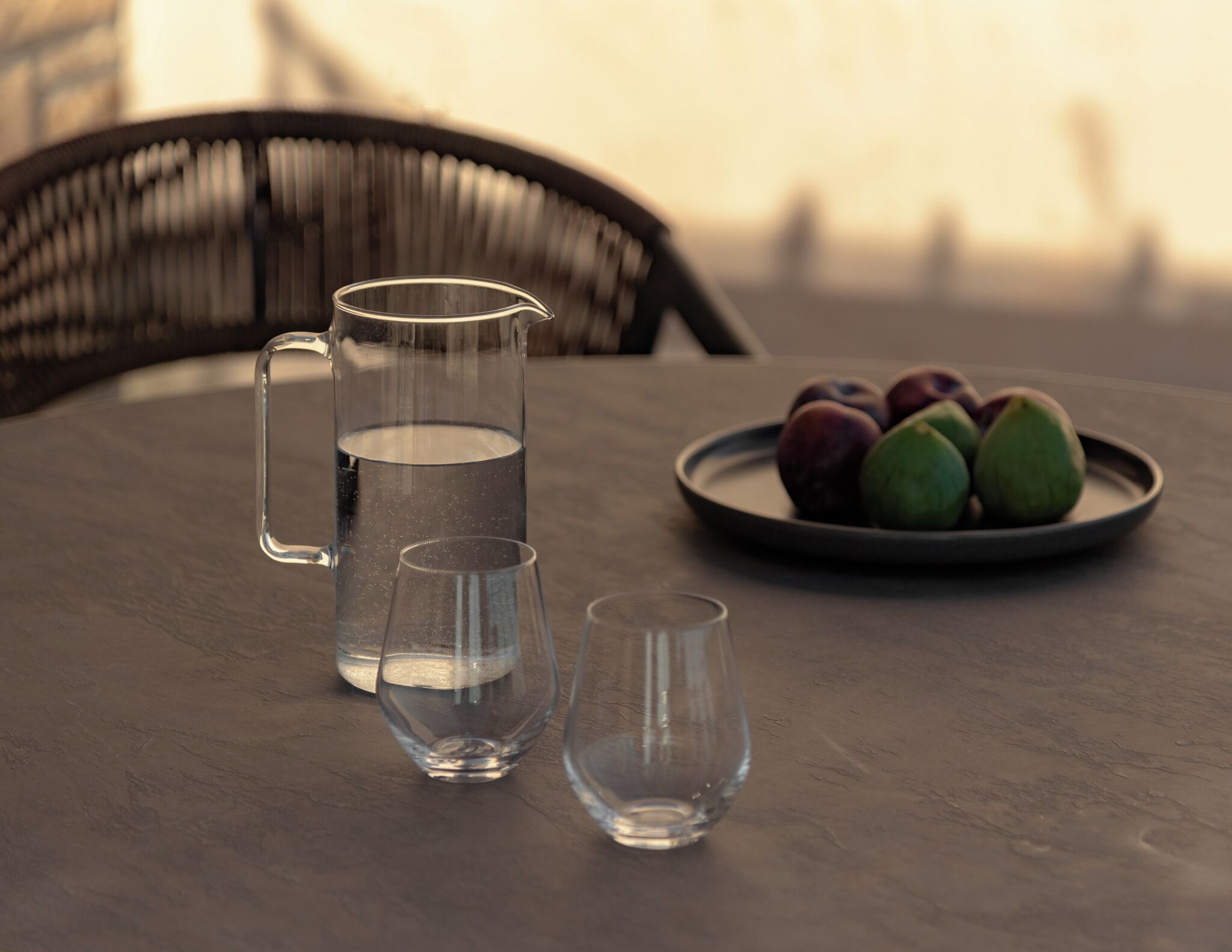 A table with a pitcher of water, two glasses, and a plate of fruit.
