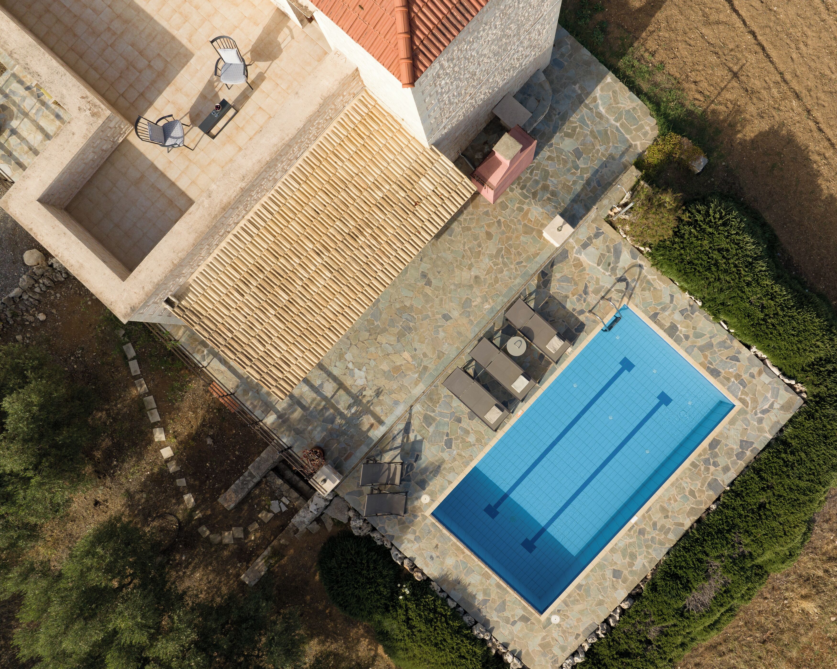 An aerial view of a property with a swimming pool, outdoor seating, and a stone patio.