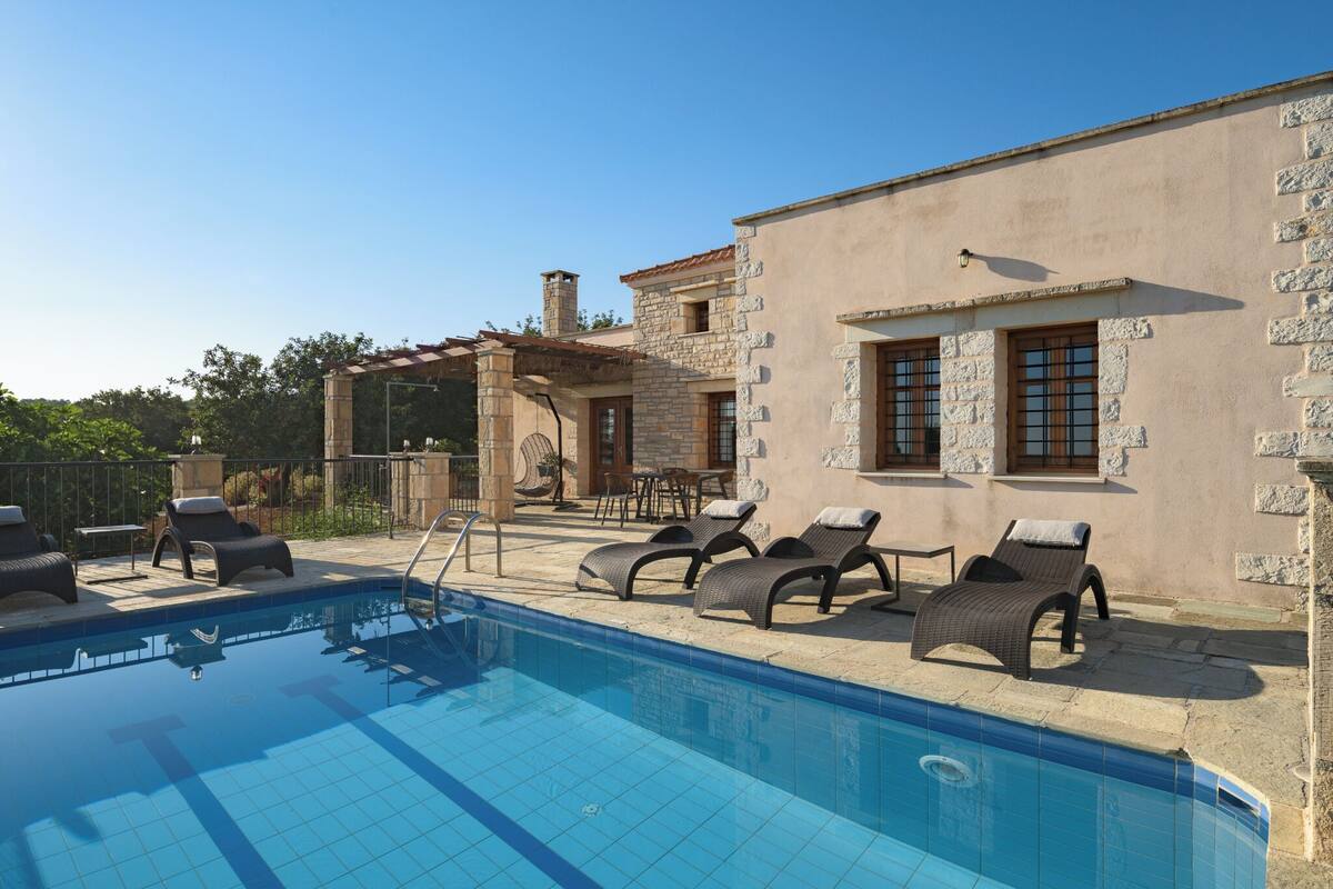 A swimming pool with lounge chairs, a stone building with windows, and a clear sky.
