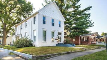 A two-story white house with a gabled roof, a front porch, and a small front yard.