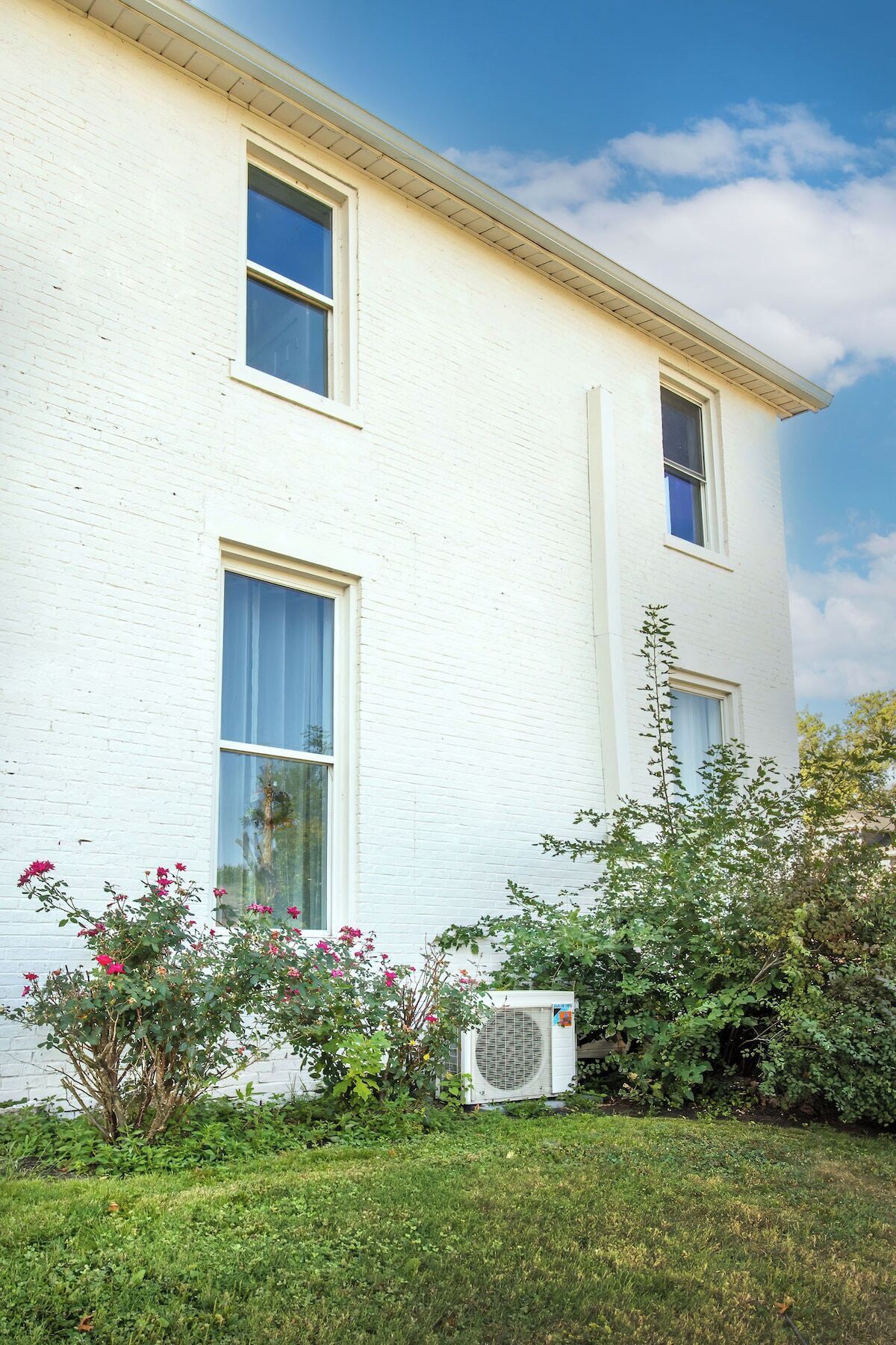 Un edificio blanco con dos ventanas y una unidad de aire acondicionado pequeña al frente.