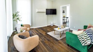 A modern living room with a flat-screen TV, a ceiling fan, and a dining area with a table and chairs.