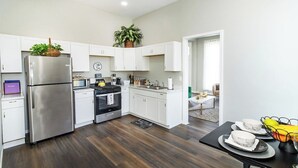 A modern kitchen with white cabinets, a stainless steel refrigerator, a microwave, and an oven. There is a dining area with a table set for two.
