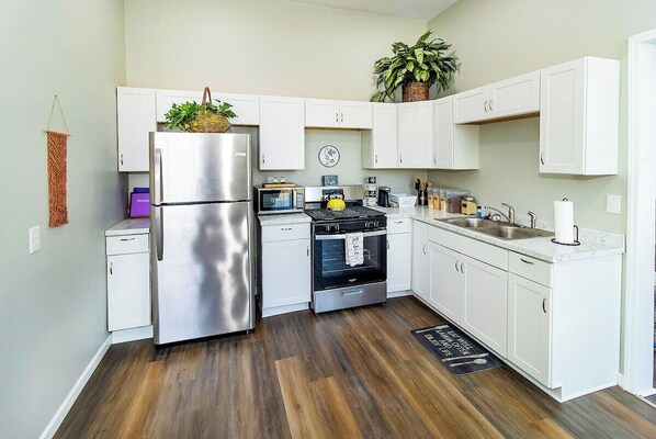 A modern kitchen with white cabinets, stainless steel appliances, and a wooden floor.