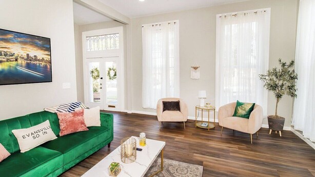 A living room with a green sofa, two armchairs, a coffee table, and a cityscape painting.