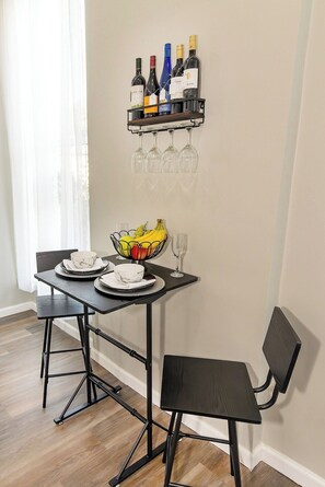 Un comedor con una mesa dispuesta para dos personas, un frutero y una botellera con botellas y copas.