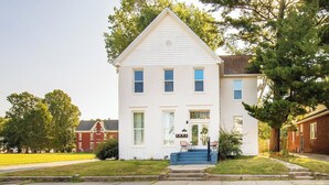 A two-story white house with a front porch, a small staircase, and a well-maintained lawn.