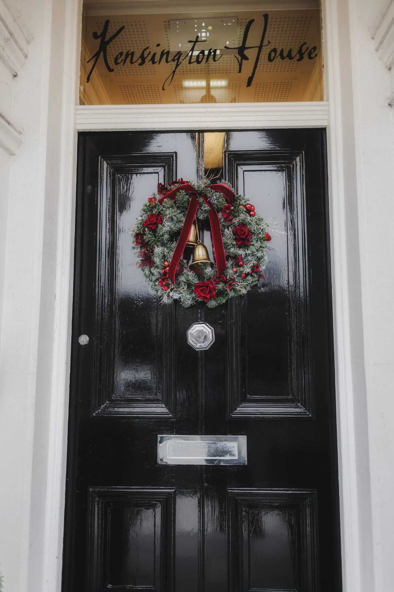 A black door with a wreath and a bell, and a sign above that reads "Kensington House".