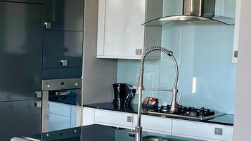 Una cocina moderna con una isla central, taburetes de bar, un lavamanos de acero inoxidable y una estufa a gas.