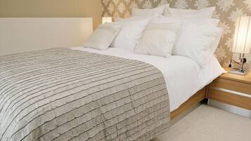 A neatly made bed with a textured blanket, a bedside lamp, and a wall with a leaf pattern.