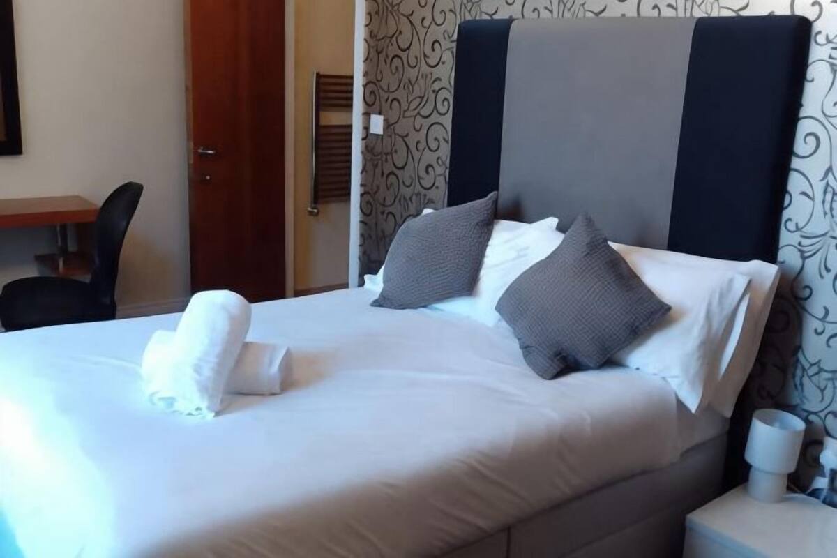 Ein Hotelzimmer mit Bett, Kissen, Nachttisch und einem Sessel.