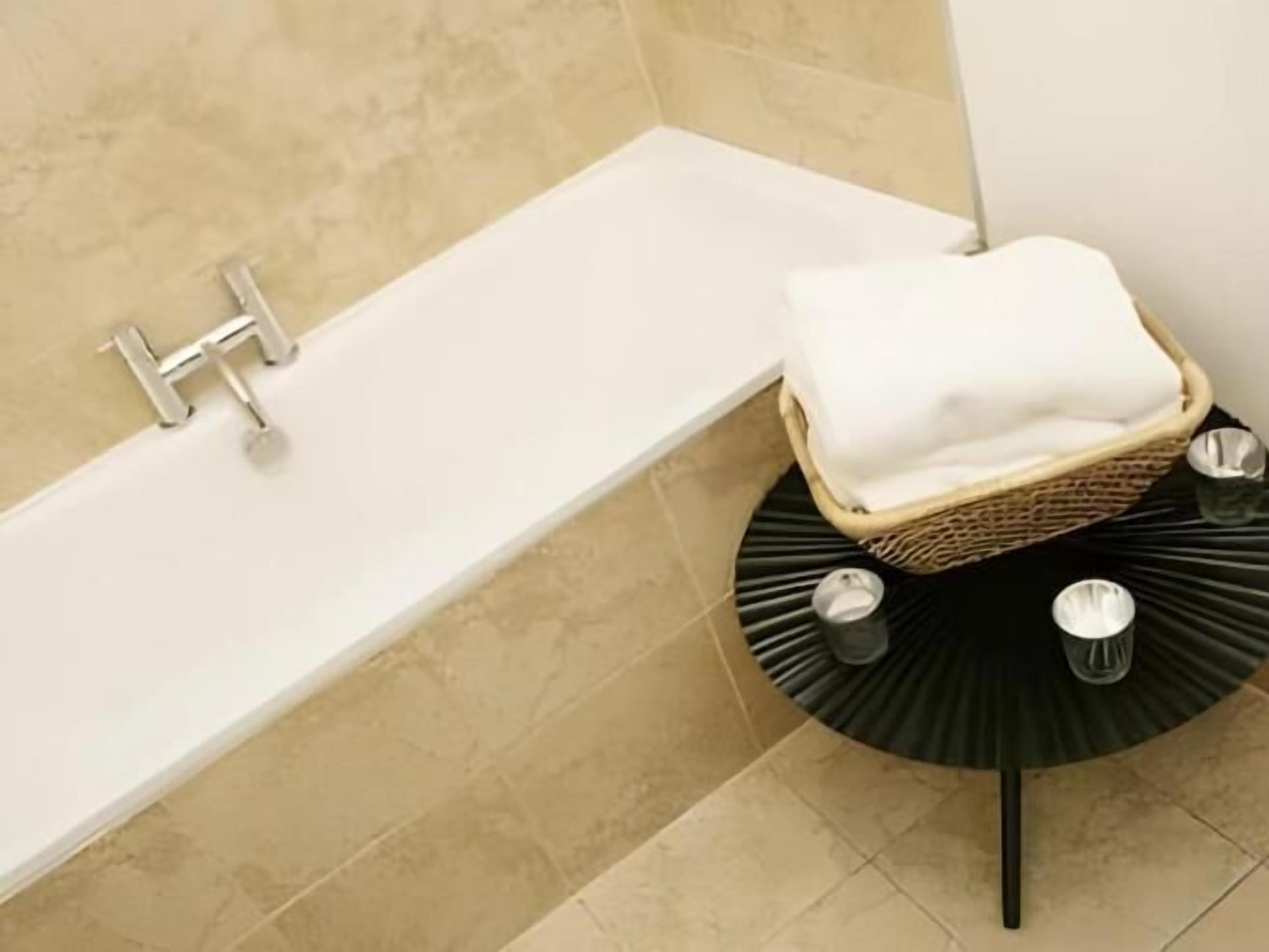 A bathroom with a bathtub, a wicker basket with a white towel, and a black round table with two metallic objects.