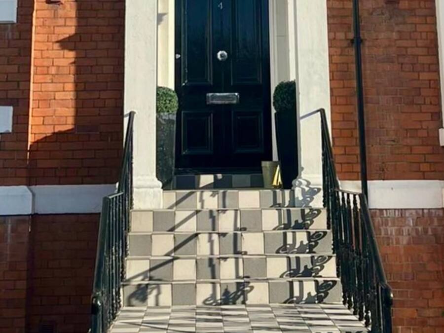 Escadaria que leva a uma porta preta com um arco branco e uma luminária acima.