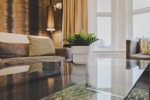 A modern living room with a glass coffee table, a potted plant, and a leather sofa.