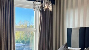 Ein Hotelzimmer mit einem großen Bett, einer Kristalllüster, gestreifter Wandgestaltung und Blick auf Bäume.