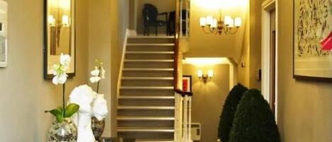 A hallway with a staircase, a dining area with a table and chairs, and wall-mounted lighting fixtures.