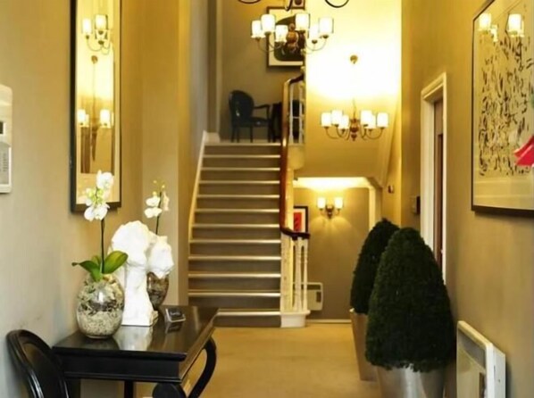 A hallway with a staircase, a dining area with a table and chairs, and wall-mounted lighting fixtures.