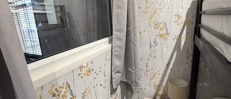 Una camera da letto con finestra, un comodino con lampada e carta da parati a motivi floreali.
