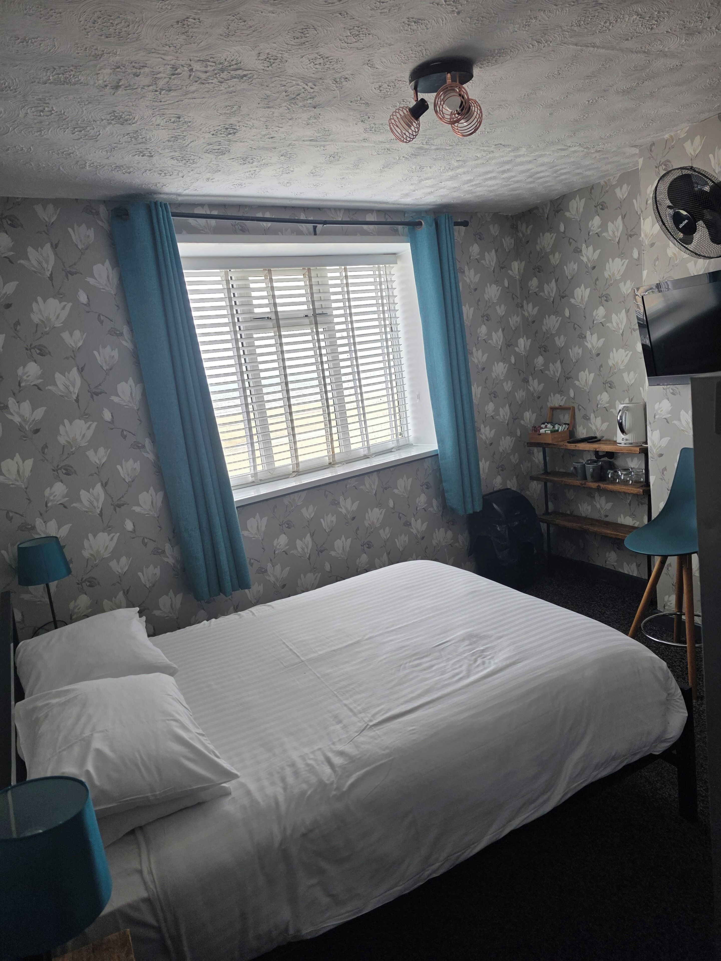 A bedroom with a bed, a window with curtains, a desk with a chair, and a ceiling fan.