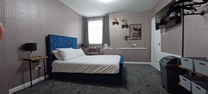 Une chambre à coucher avec un lit, un bureau, une chaise, une télévision et une fenêtre.