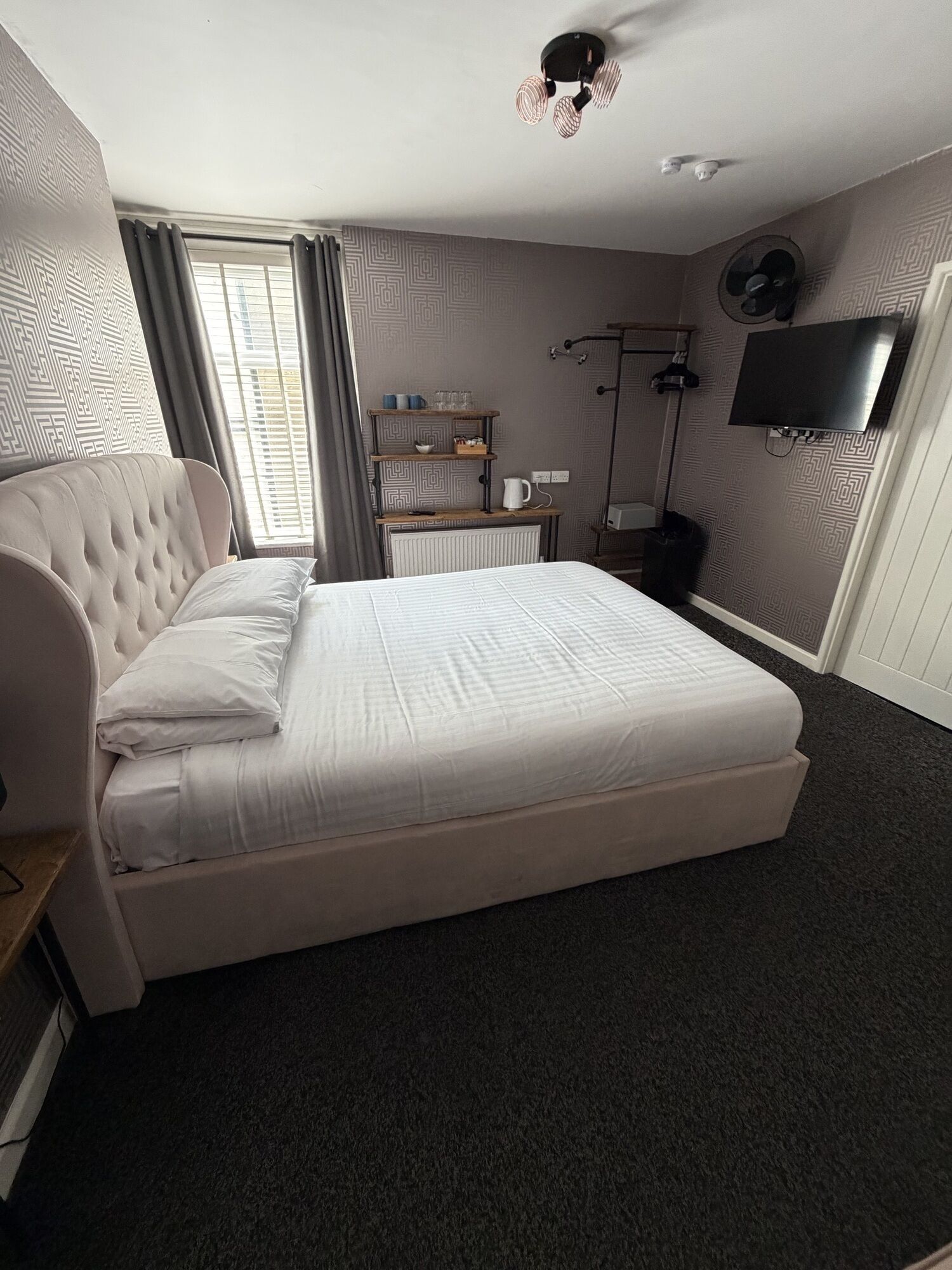Una habitación de hotel con una cama grande, un televisor montado en la pared y una ventana con cortinas.
