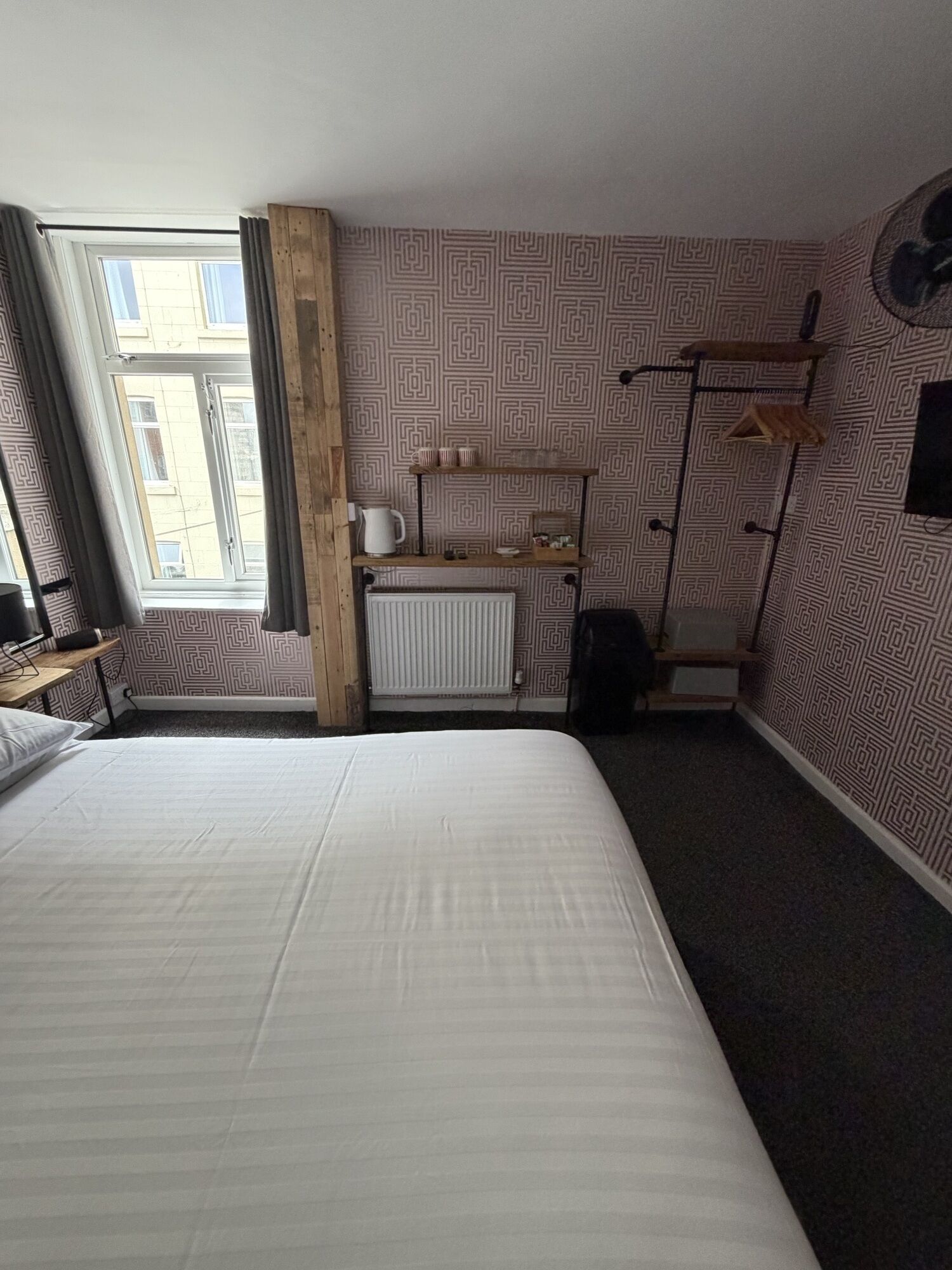 Et hotelværelse med en stor seng, en radiator, et skrivebord med stol og et vindue med gardiner.
