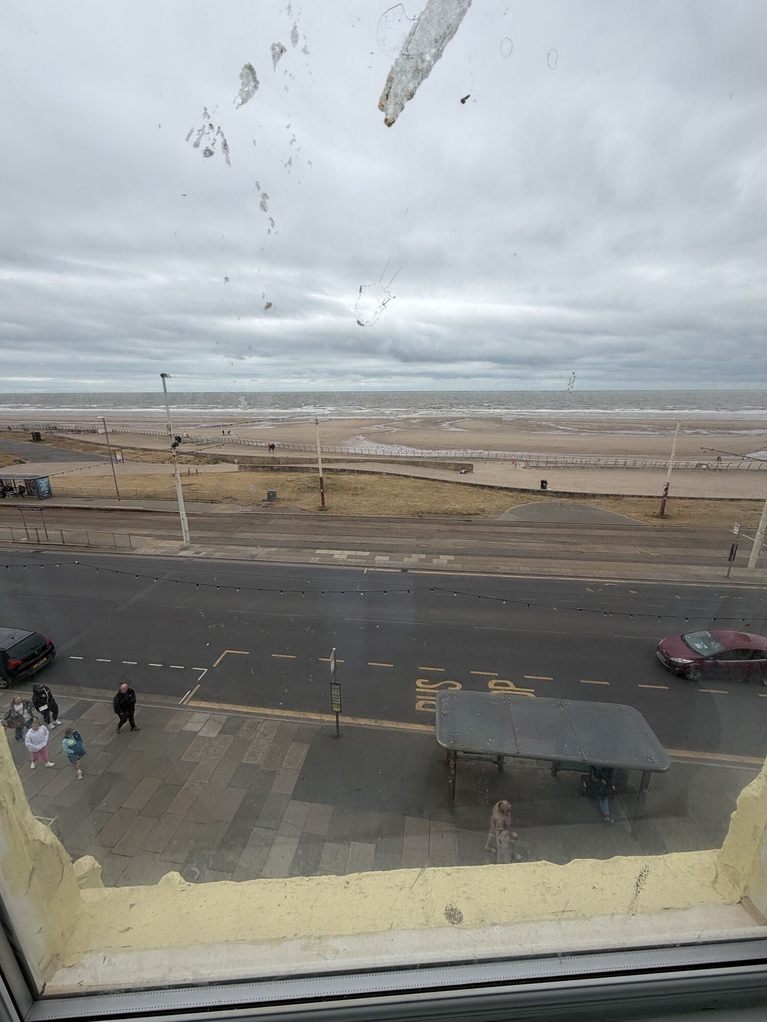 A view from a window overlooking a beach with a parking area and a bus stop.