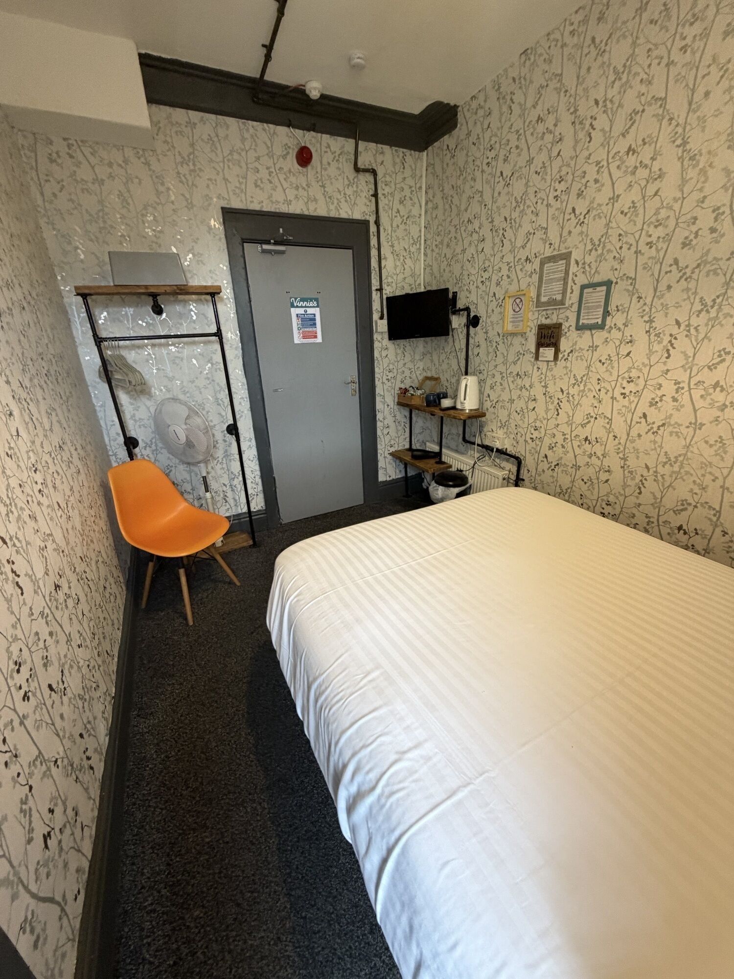 A hotel room with a bed, a desk with a chair, a television, and a radiator.
