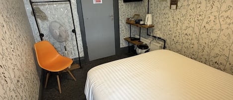 A hotel room with a bed, a desk with a chair, a television, and a radiator.