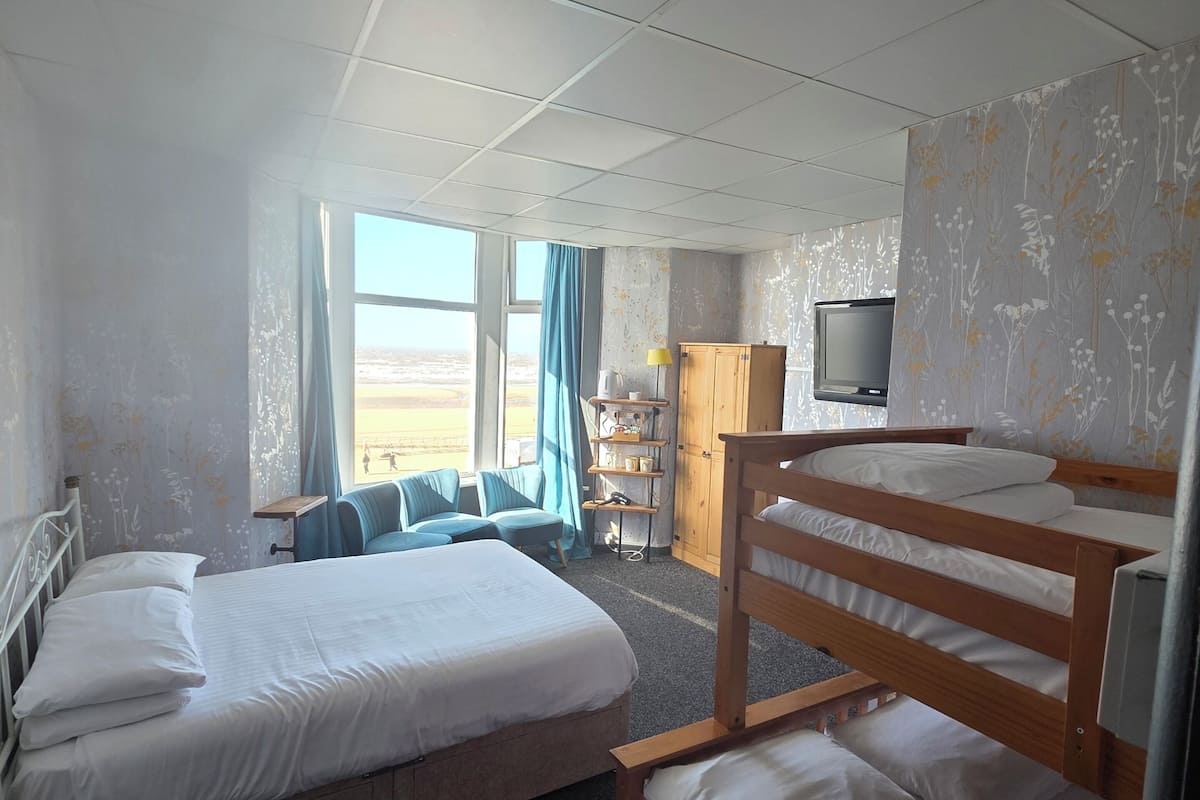 A hotel room with two beds, a television, a desk with a lamp, and a view of the outdoors.