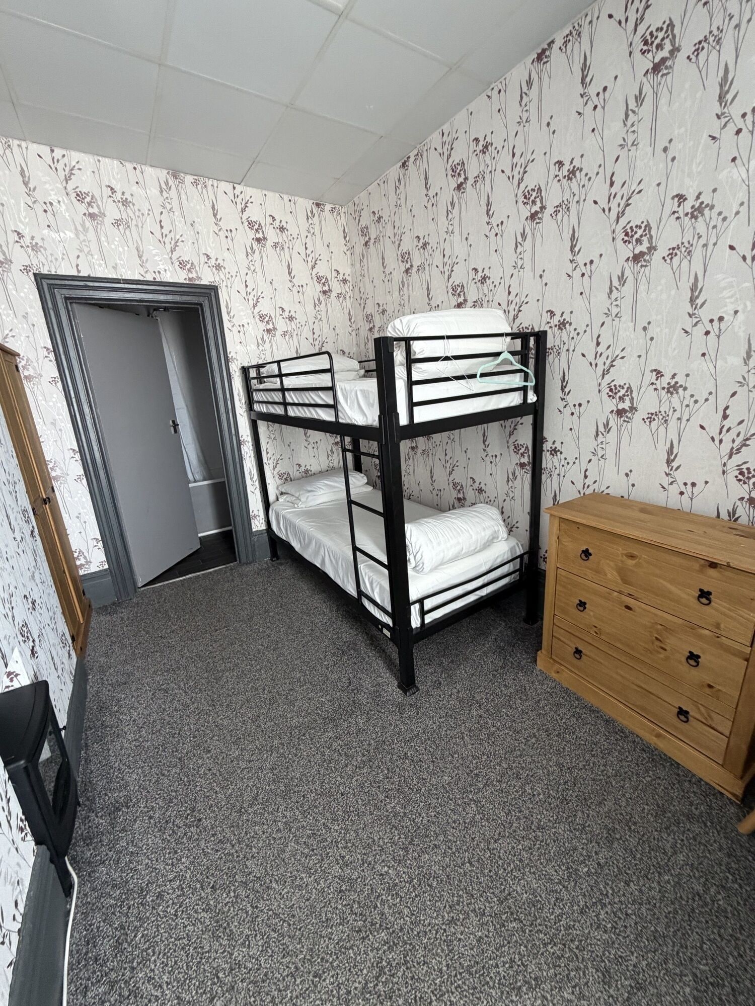 A bunk bed room with a wooden dresser and floral wallpaper.