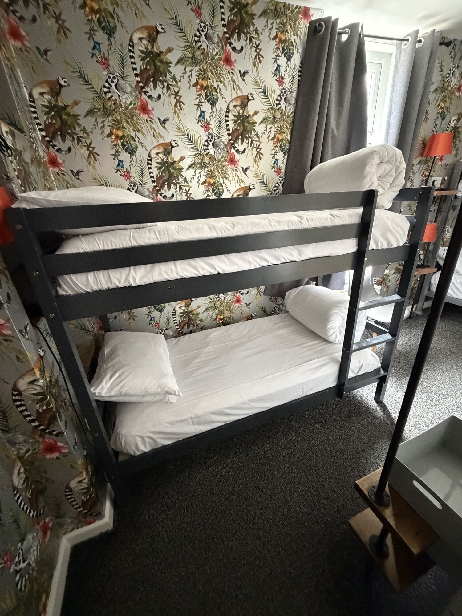 A bunk bed with white bedding in a room with floral wallpaper and a grey curtain.