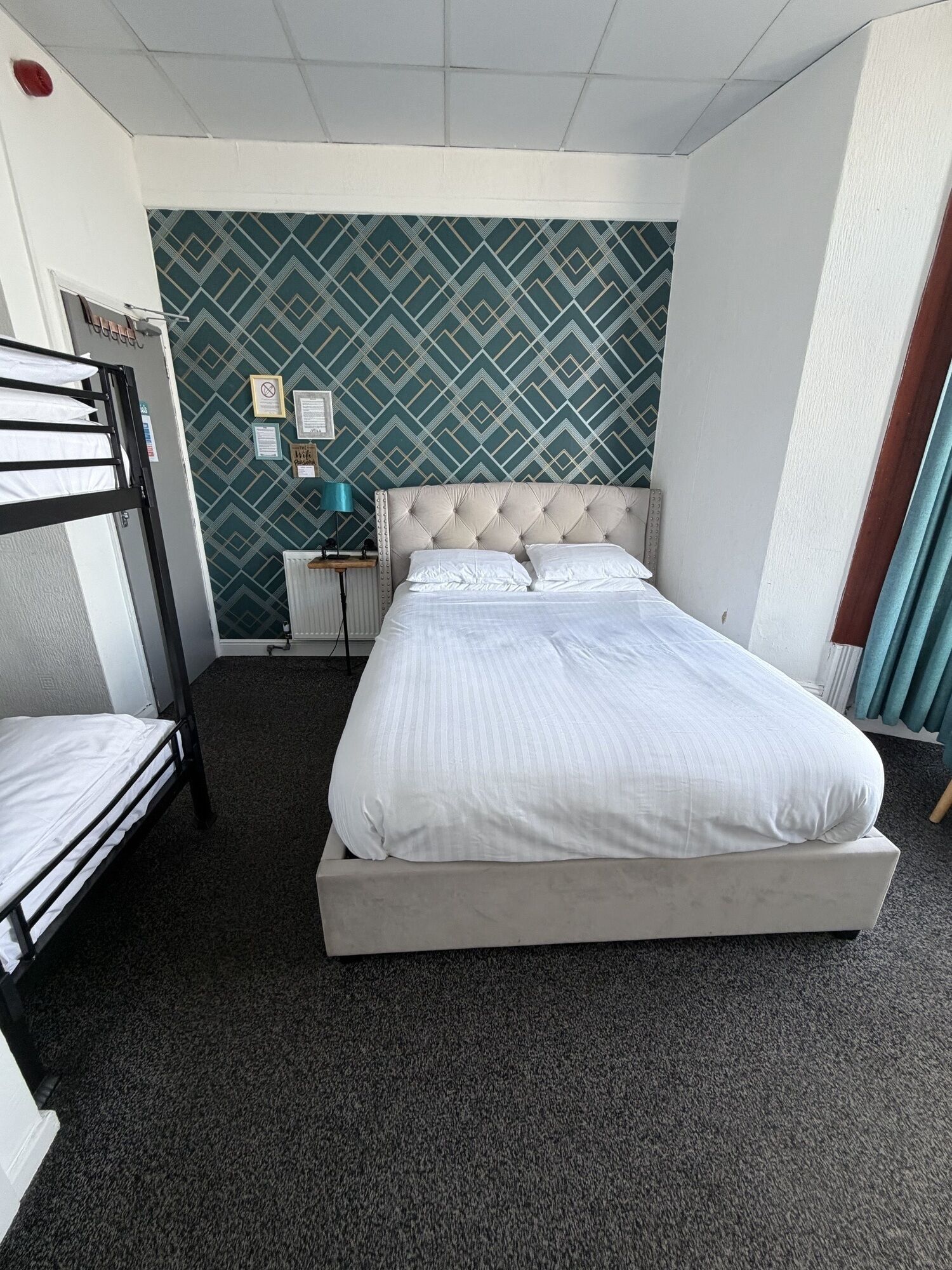 Habitación de hotel con una cama grande, una litera, un radiador y un papel tapiz estampado.
