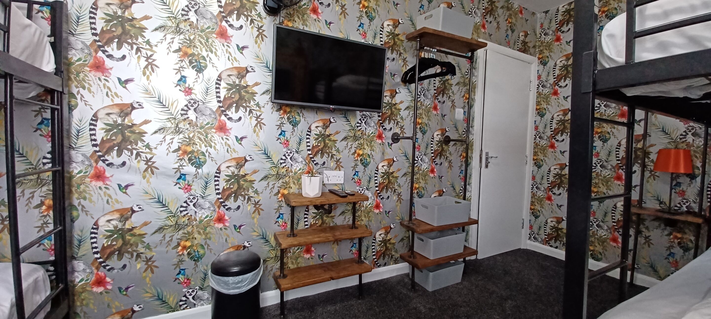 A room with a bunk bed, a TV mounted on the wall, a shelf with storage bins, and a trash bin.