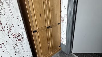 A corner with a wooden wardrobe against a floral wallpaper, a grey carpet, and a grey door.