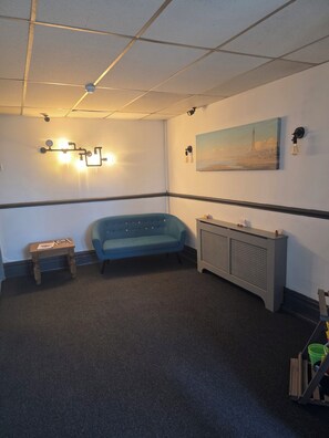 A room with a blue sofa, a small wooden table, a radiator, and a painting on the wall. - Vinnies Family Hotel (Blackpool)