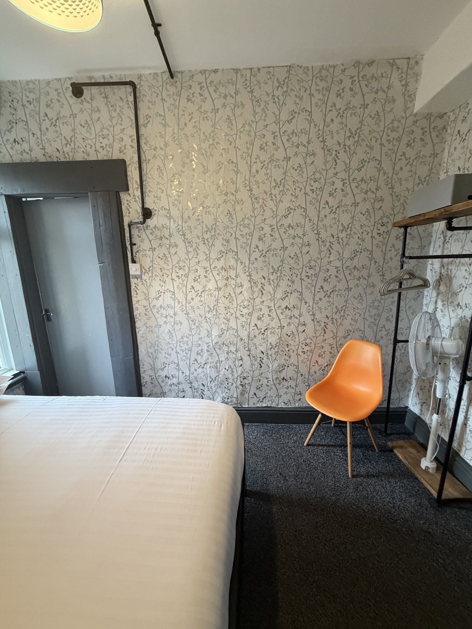 Une chambre d’hôtel avec un lit, une chaise, une statue et un mur orné d’un motif floral.