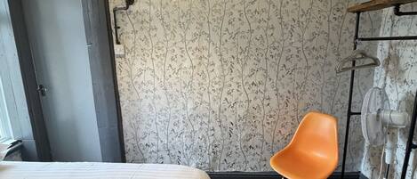 A hotel room with a bed, a chair, a statue, and a wall with a floral pattern.