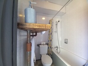 Ein Badezimmer mit Holzregal über der Toilette, einer Dusche und einem Toilettenpapierhalter.