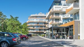En moderne bygning med flere etager, altaner, en restaurant og parkerede biler.