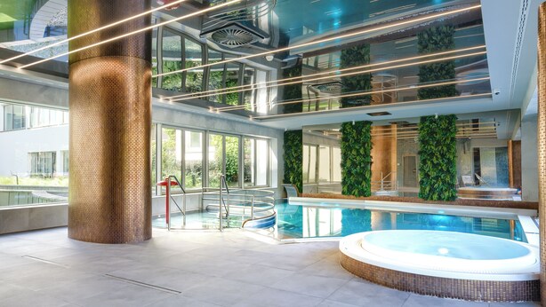 A modern indoor swimming pool area with a hot tub, glass walls, and green vertical gardens. - Apartamenty Sun & Snow Lividus (Swinoujscie)