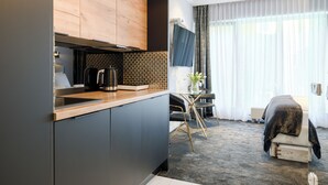 A modern kitchen with a wooden countertop, a coffee machine, and a tiled backsplash. There is a dining area with a table and chairs, and a bed with a black cover. - Apartamenty Sun & Snow Lividus (Swinoujscie)