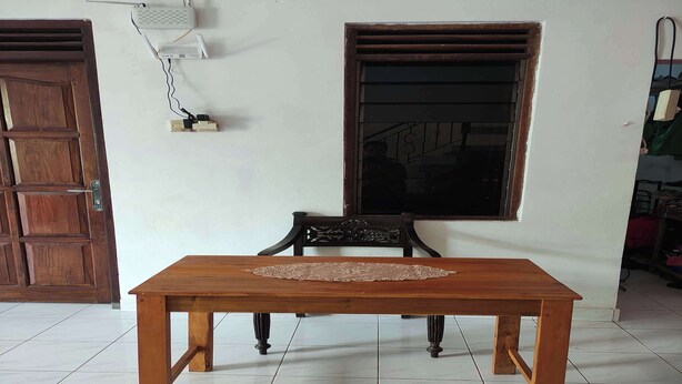 Une table de salle à manger en bois, avec un set de table, deux fenêtres et une prise électrique fixée au mur.
