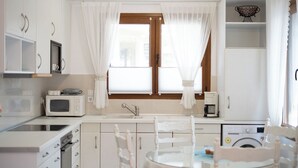 Una cocina moderna con armarios blancos, microondas, cafetera y lavadora.