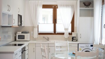 Uma cozinha moderna com armários brancos, micro-ondas, cafeteira e máquina de lavar roupa.