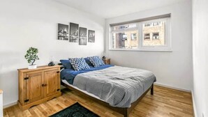A bedroom with a bed, wooden wardrobe, and a window with a view of buildings. - The Elden - No.3 (London)