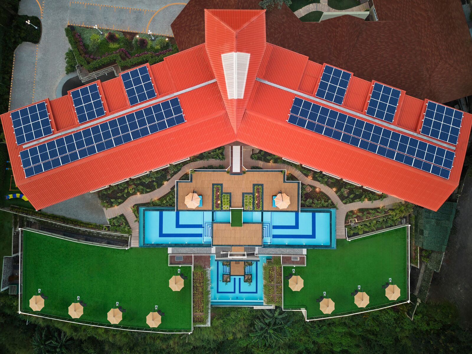 A modern hotel with a central swimming pool, multiple guest rooms, and solar panels on the roof.